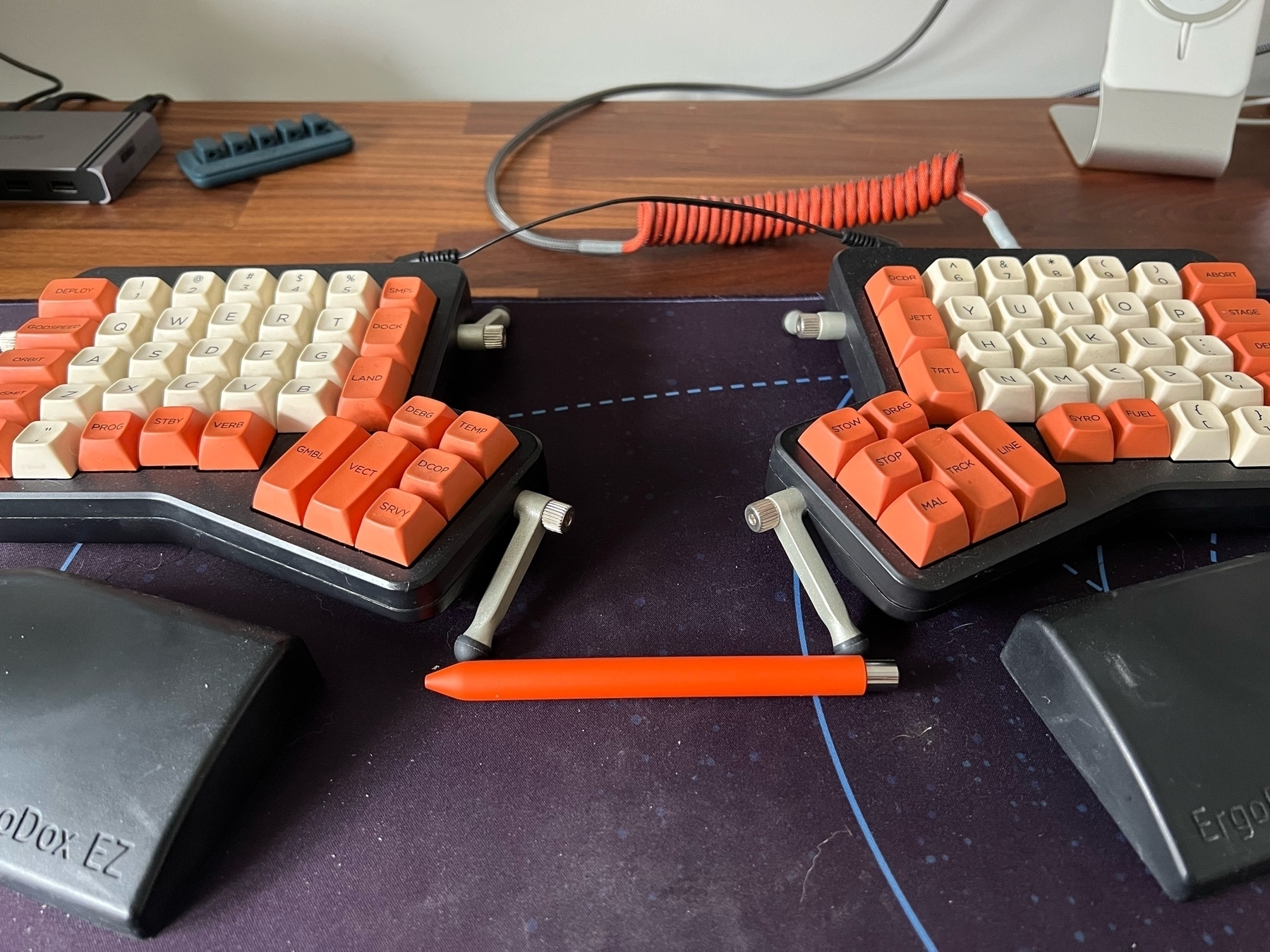 Ergodox EZ keyboard with orange and cream keycaps and a matching Studio Neat Mark One orange pen.