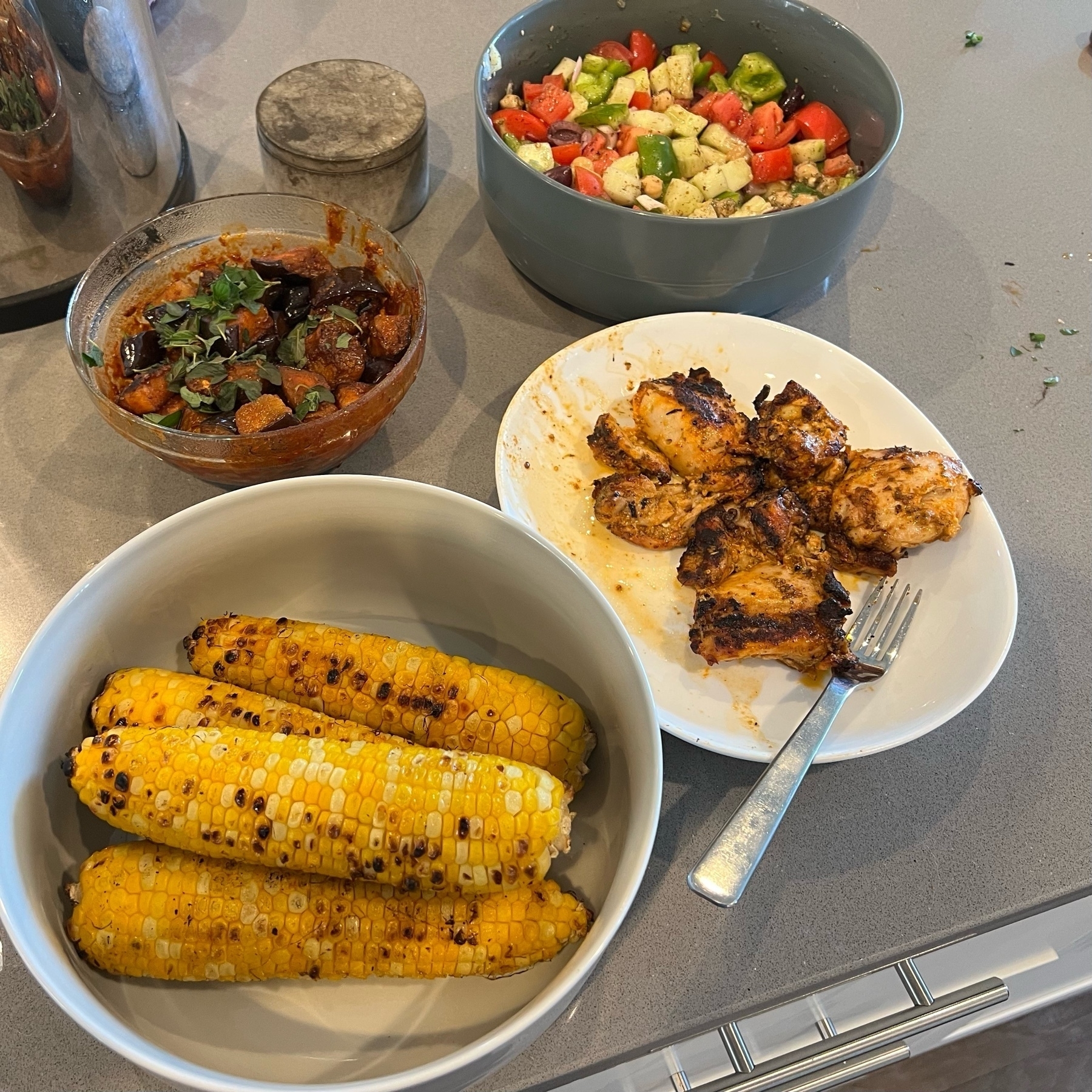 Greek salad, roasted eggplant in harissa, grilled chicken thighs, and grilled corn