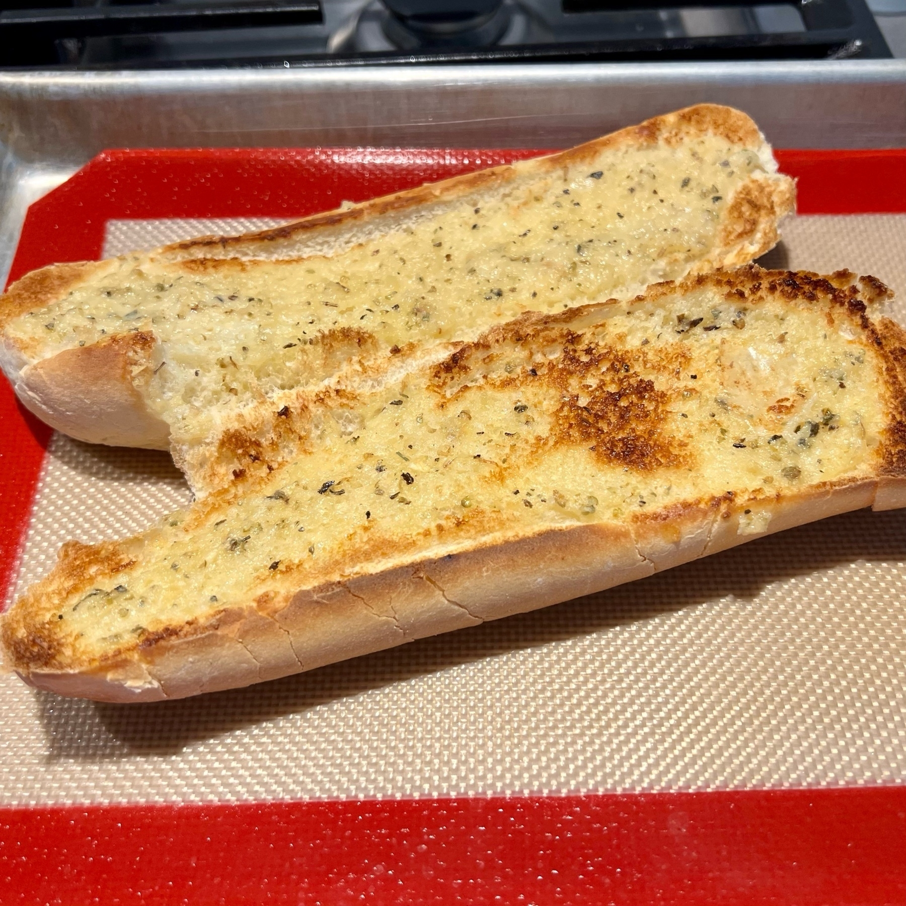 Garlic bread on a red and beige sil pad and quarter sheet.