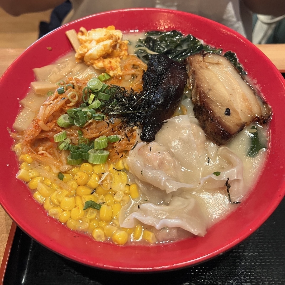 Ramen in a red bowl with pork, corn, and dumplings.