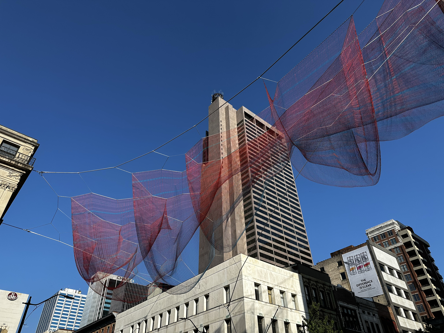 Red and blue netting twisted together against the backdrop of a clear sky and the city behind.