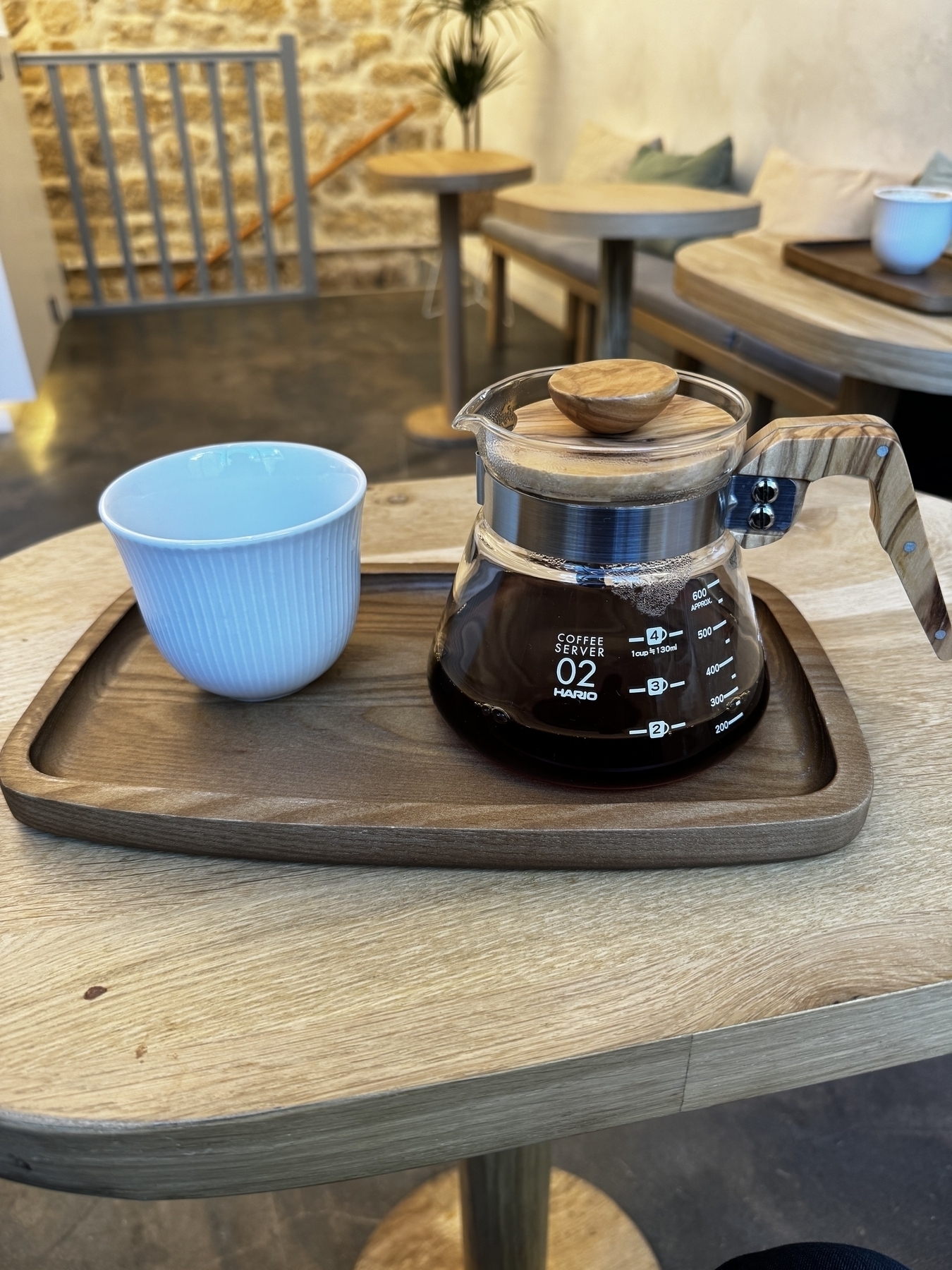 Hario coffee server on a wood tray with one cup of coffee.