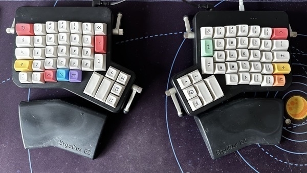 Ergodox EZ keyboard with primarily beige keycaps that are designed like old Apple-style keys and a few keys with pastel-like coloring
