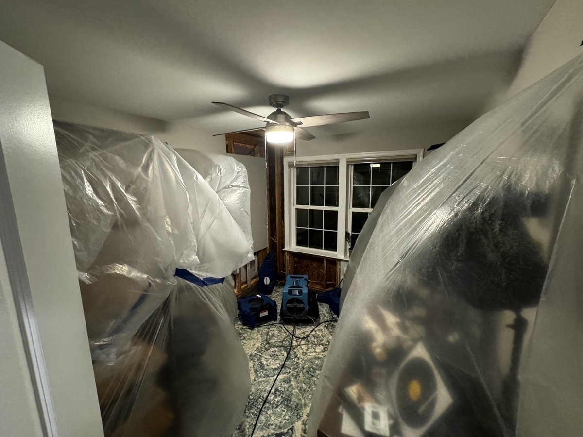 Two plastic sheets covering most of my office, with walls in the back corner with substantial portions of drywall removed. There are blue blowers and dehumidifiers in the center of the room